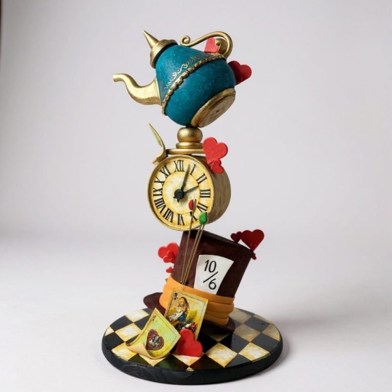 Whimsical Alice in Wonderland–themed cake featuring a tilted brown Mad Hatter hat with 10/6 card, a gold clock with Roman numerals, and a blue and gold teapot balanced on top, decorated with red hearts, playing cards, and a black-and-gold checkerboard base