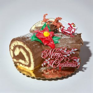 Chocolate yule log cake with “Merry Christmas” decoration, Santa sleigh and reindeer topper, and festive holiday design.