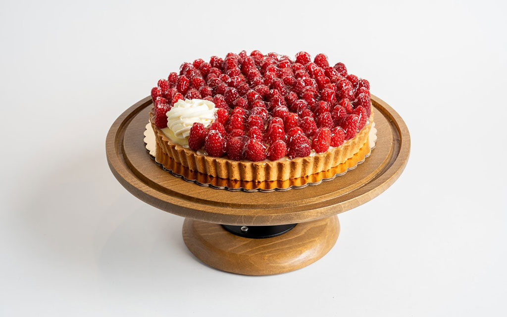 Fresh raspberry tart with pastry cream on wooden cake stand as elegant 4th of July dessert ideas centerpiece