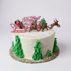 Festive Christmas cake featuring Santa sleigh and reindeer topper with winter tree decorations and white buttercream frosting.