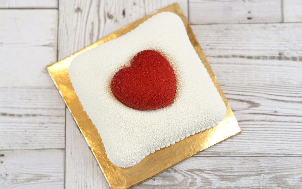 Mother's Day dessert idea with white square cake topped with red heart decoration on gold board