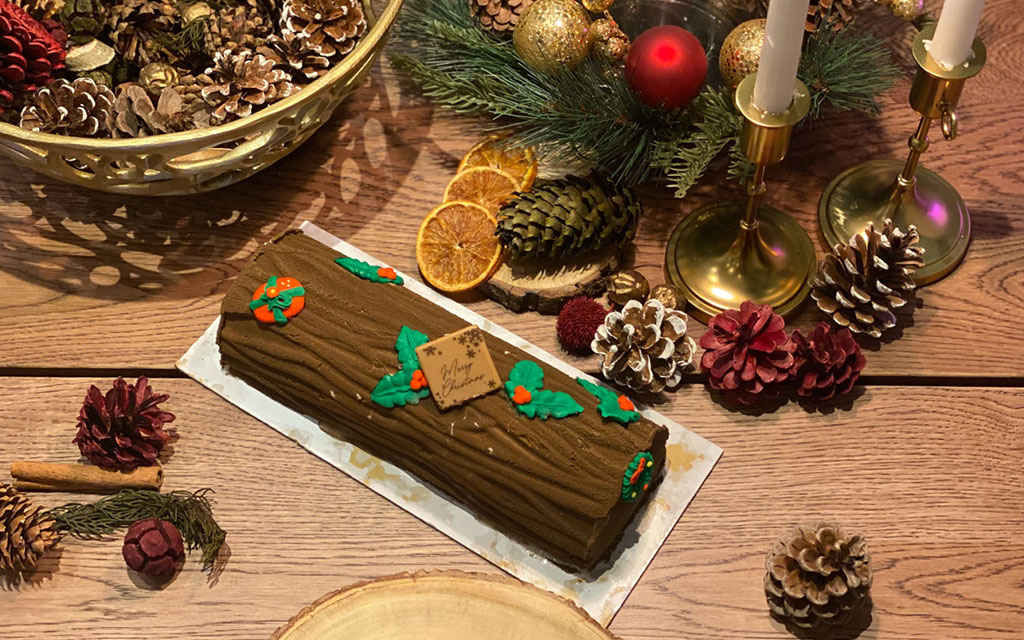 Chocolate yule log cake decorated with holly and berries on festive table with pinecones and christmas ornaments