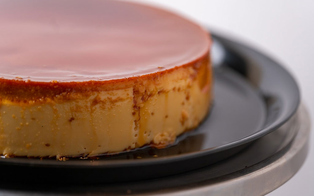Creamy flan dessert with caramel topping on black plate showing smooth custard texture and golden caramelized surface