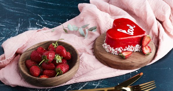 Valentines dessert ideas featuring red heart shaped cake with love inscription and fresh strawberries on pink linen, romantic celebration treats
