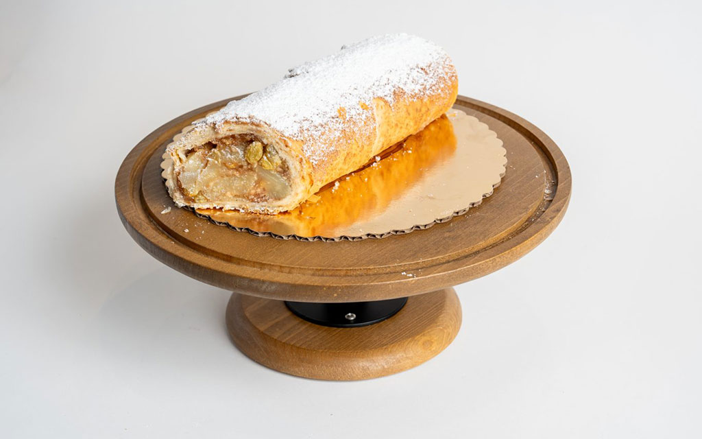 Apple strudel dusted with powdered sugar on wooden cake stand, elegant fall dessert idea