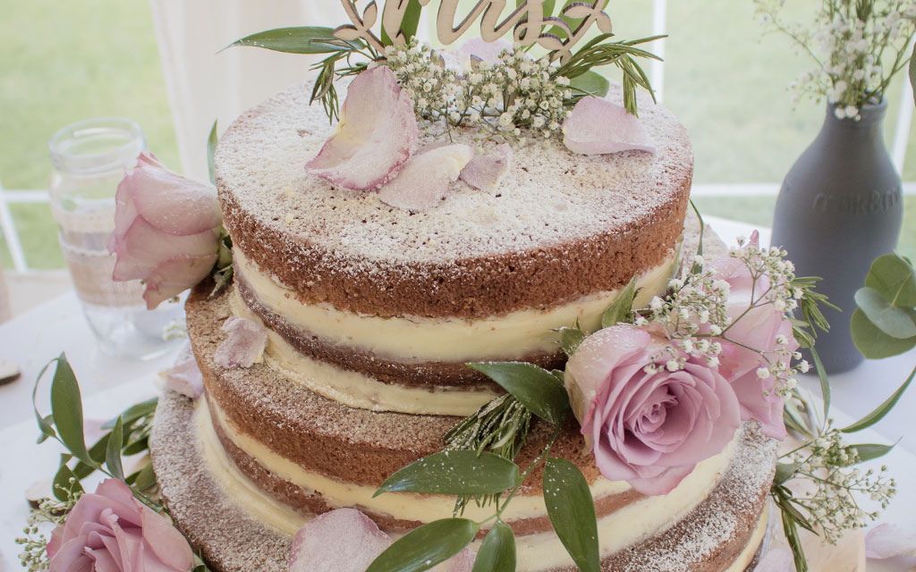 Naked wedding cake with vanilla layers showing different wedding cake flavors and fresh pink roses