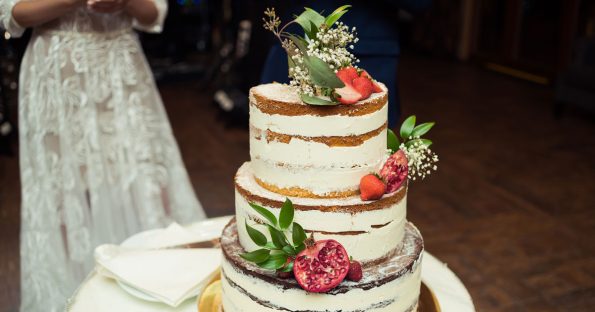 Three-tier naked wedding cake with fresh strawberries and greenery at real wedding reception
