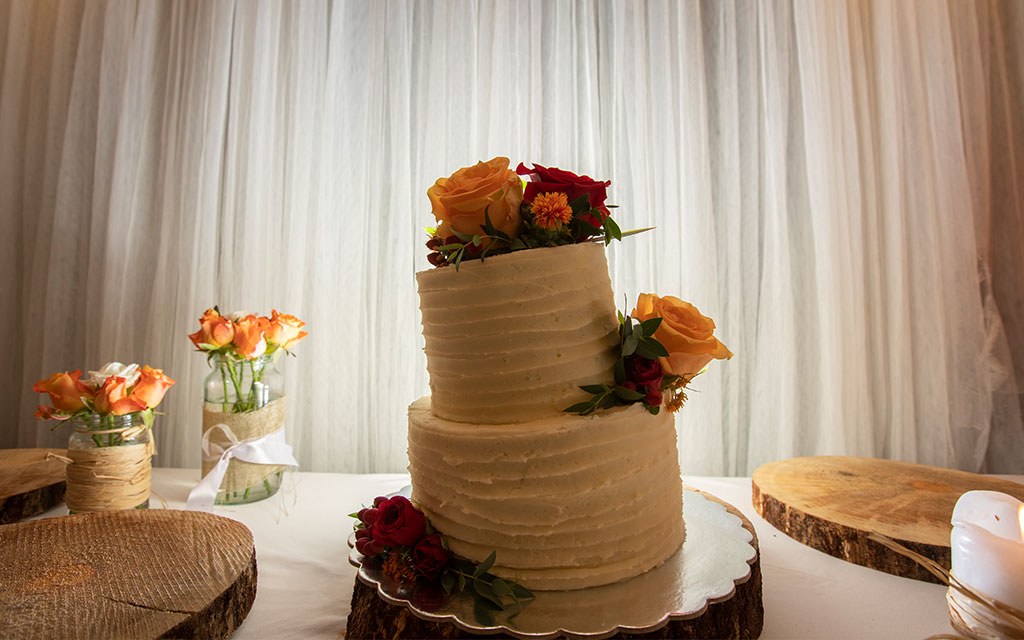 Two-tier spring wedding cake with textured buttercream and fresh flowers on rustic wooden stand at indoor reception