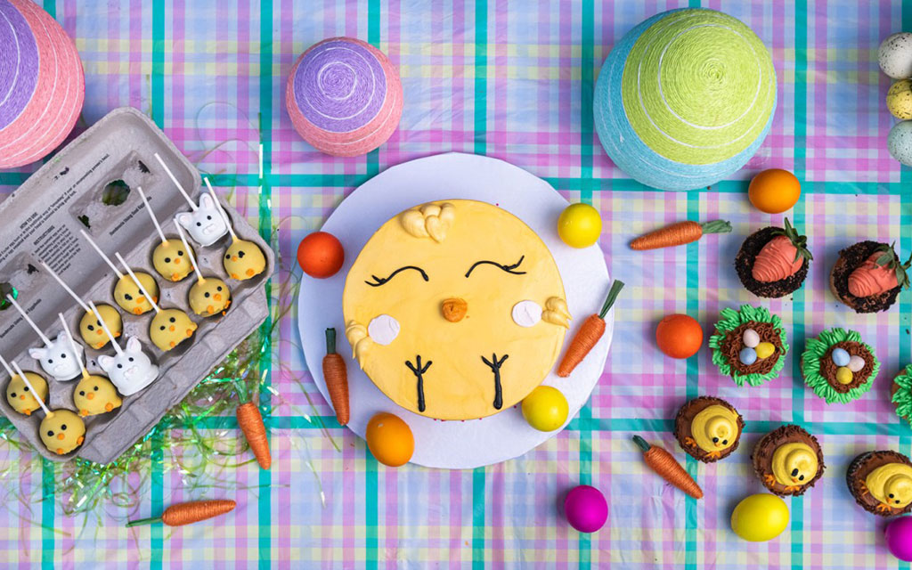 Seasonal desserts for Easter including bunny face cake, chick cake pops, and spring-themed cupcakes on colorful tablecloth