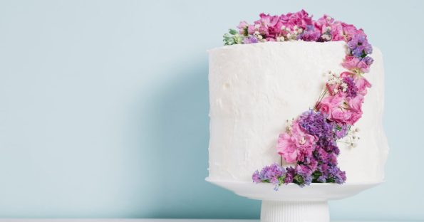 Square spring wedding cake featuring cascading fresh flowers in pink and purple tones on white pedestal cake stand