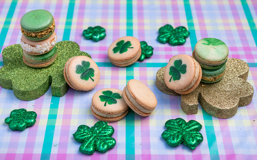 Green and gold shamrock macarons arranged on colorful plaid surface as festive St Patrick's Day dessert ideas
