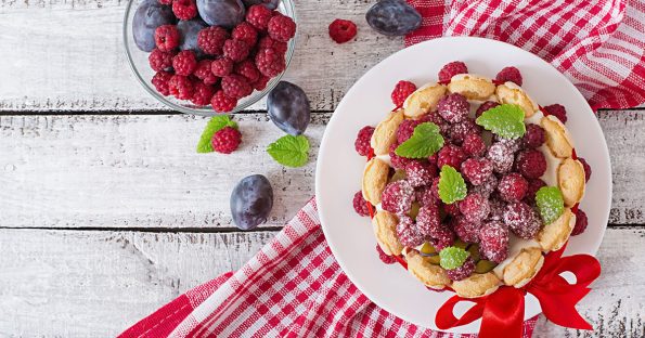 Fresh berry tart with raspberries and plums on rustic table, a colorful summer dessert idea overhead view