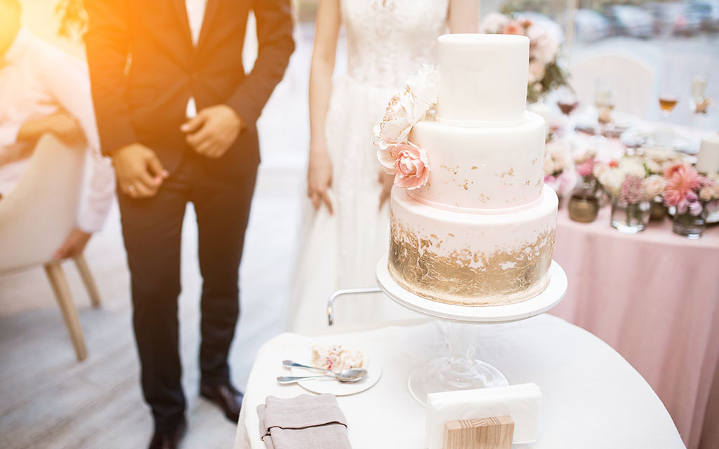 Summer wedding cake with blush pink tiers, gold leaf accent, and peach sugar flowers at elegant reception