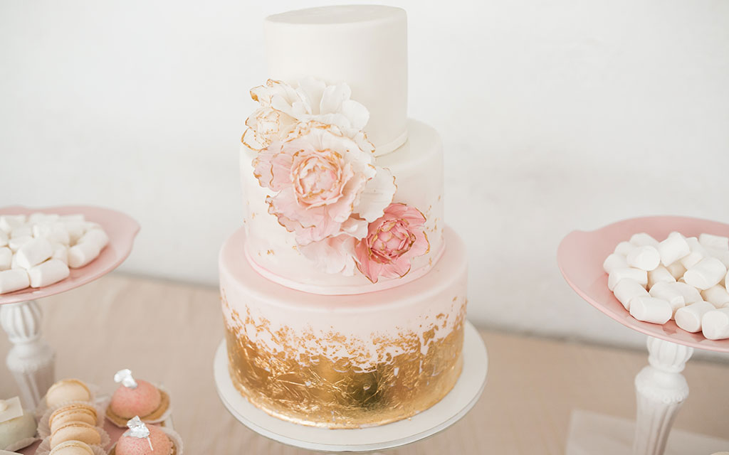 Summer wedding cake with blush pink tiers, gold leaf accent, and elegant sugar flowers on romantic dessert table
