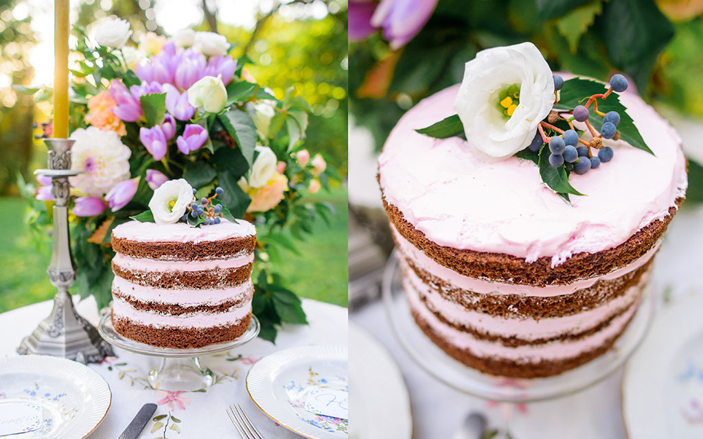 Summer wedding cake in naked style showing exposed chocolate layers with berry filling, fresh flowers, and blueberries