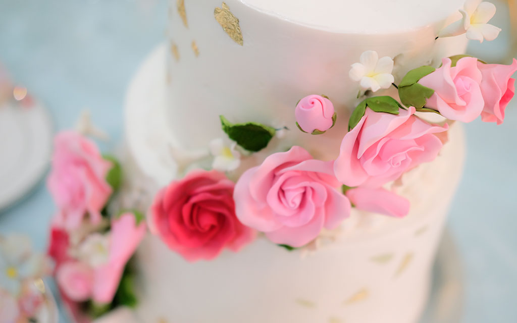 Summer wedding cake detail showing handmade sugar roses in pink and coral with gold leaf accents on pastel tiers