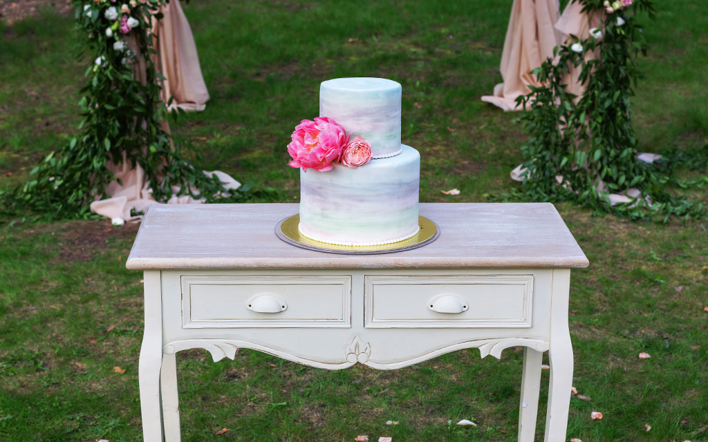 Summer wedding cake with watercolor buttercream in soft pastels and fresh pink peonies at outdoor garden reception