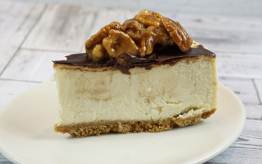 Creamy pie slice topped with chocolate ganache and caramel pecans, a decadent thanksgiving dessert on graham cracker crust