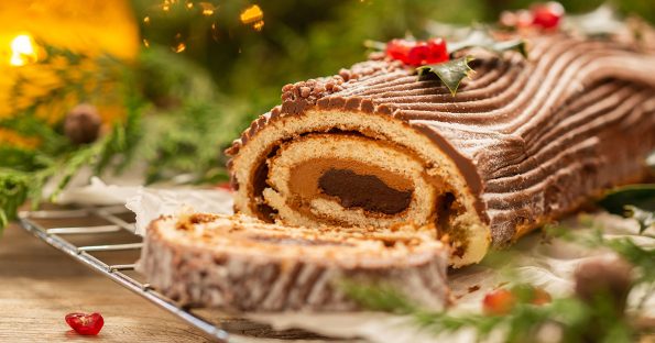 Chocolate yule log cake with buttercream frosting and holly decorations sliced on cooling rack with festive background