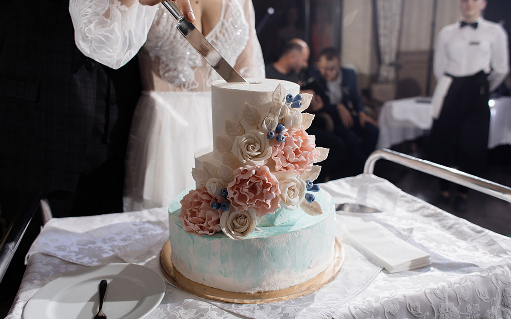 Bride cutting wedding cake at reception showing elegant two-tier design with buttercream floral decoration