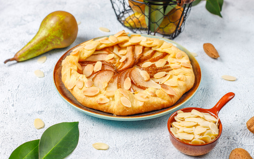Rustic pear tart topped with sliced almonds, a simple winter dessert idea using seasonal fruit and buttery crust
