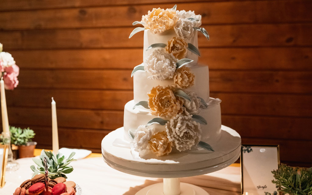Four-tier fall wedding cake with cascading sugar flowers in cream and gold tones at rustic barn venue