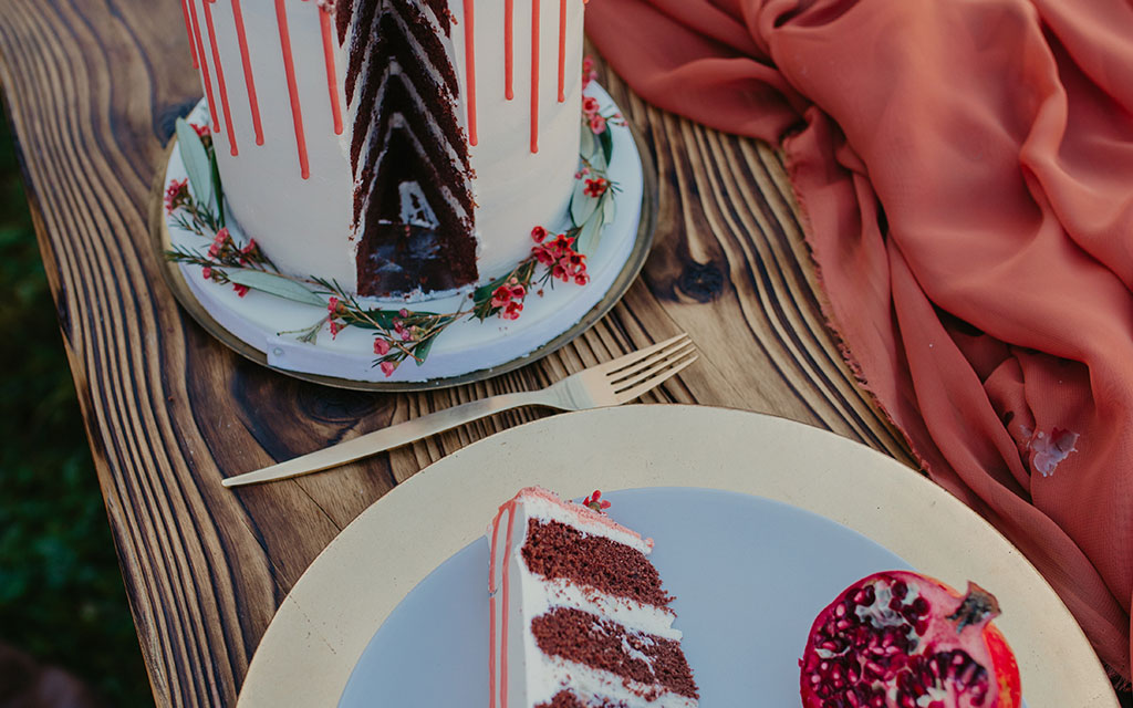 Chocolate fall wedding cake slice showing layers with white frosting, red drip, and pomegranate garnish