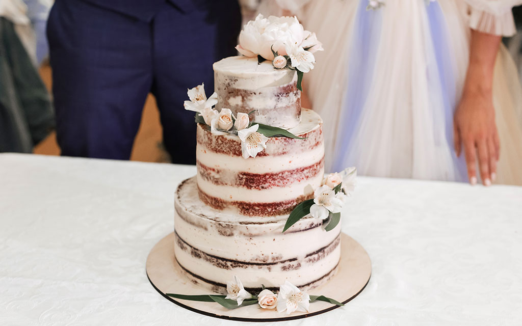 Three-tier naked wedding cake with white peonies and blush roses at wedding reception