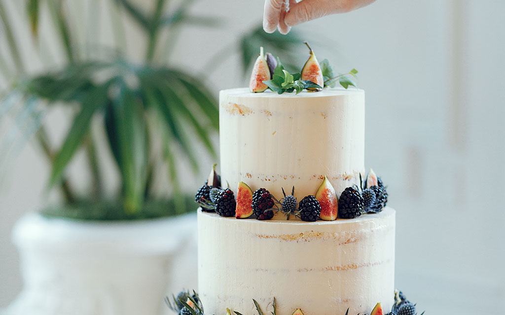 Two-tier semi-naked wedding cake decorated with fresh figs, blackberries, and greenery