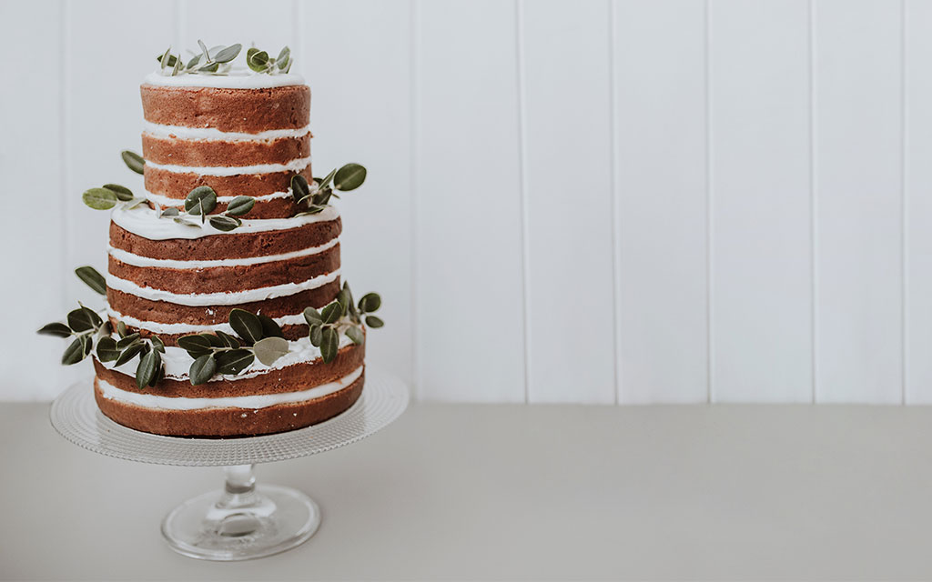 Three-tier naked wedding cake with white buttercream and eucalyptus greenery on white cake stand
