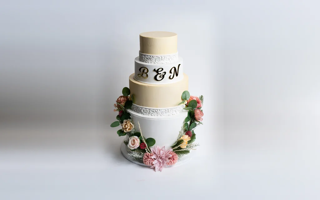 Four-tier custom wedding cake by Mia's Brooklyn Bakery with a gold B & N monogram, scrollwork bands and a flower garland