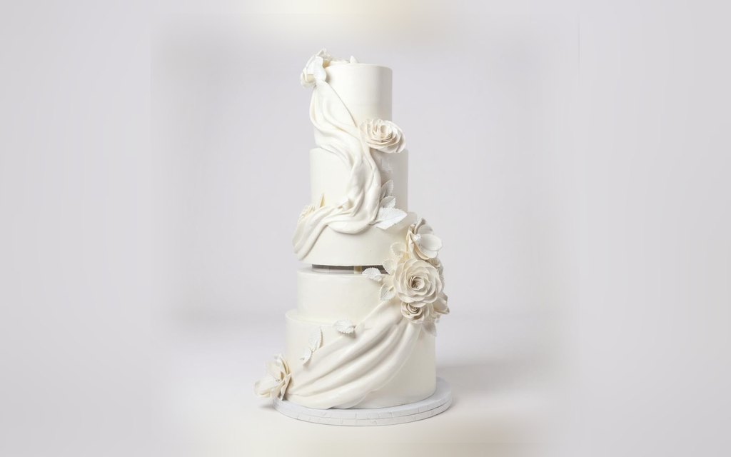 Five-tier white wedding cake by Mia's Brooklyn Bakery with draped fondant swags and handmade sugar roses