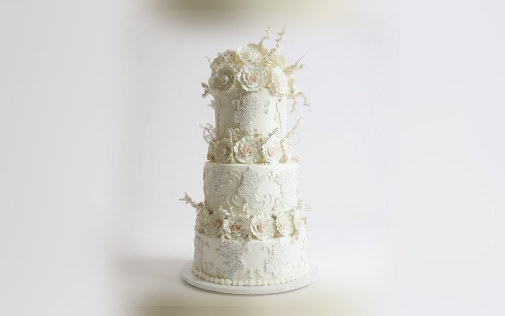 Three-tier ivory wedding cake by Mia's Brooklyn Bakery with piped lace panels and blush sugar roses