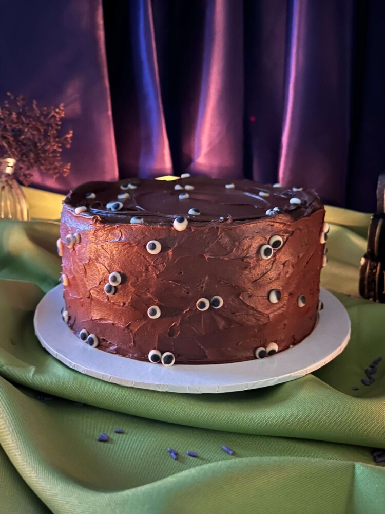 Eyeball Cake Side View, Mia's Bakery Eyeball Cake in chocolate frosting with candy eyeballs on a green Halloween table, Mia's Bakery