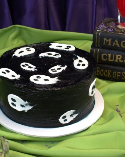Round Halloween cake in black frosting with little white ghosts on the top and sides, Mia's Bakery