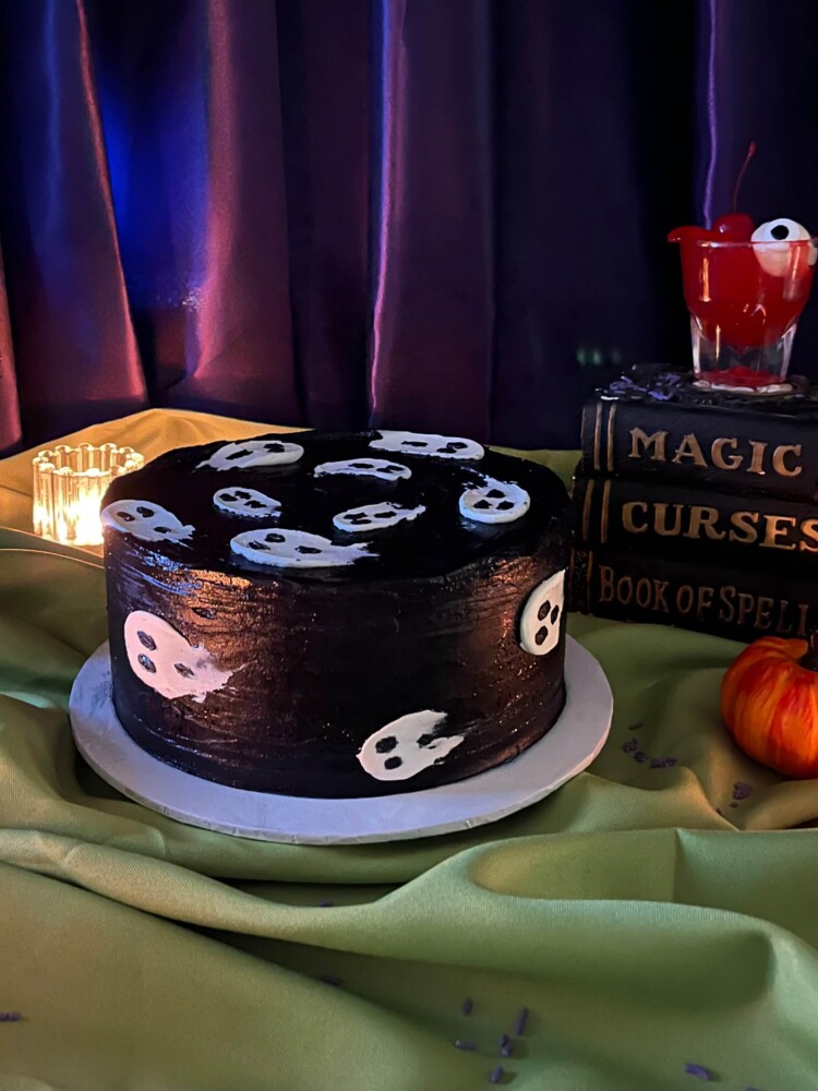 Ghosts Cake Halloween Scene, Mia's Bakery Ghosts Cake in black frosting with white ghosts, beside spell books and a small pumpkin, Mia's Bakery