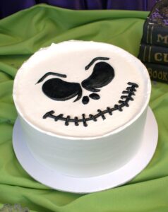 Round white buttercream cake with a grinning skeleton face piped in black, Mia's Bakery