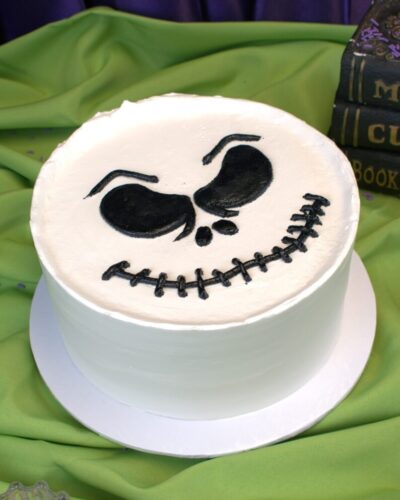 Round white buttercream cake with a grinning skeleton face piped in black, Mia's Bakery
