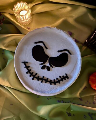 Top view of a white buttercream cake with a grinning skeleton face piped in black, Mia's Bakery