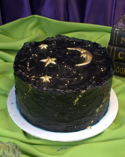 Round black frosted Halloween cake with a gold crescent moon, gold stars and gold flecks, Mia's Bakery