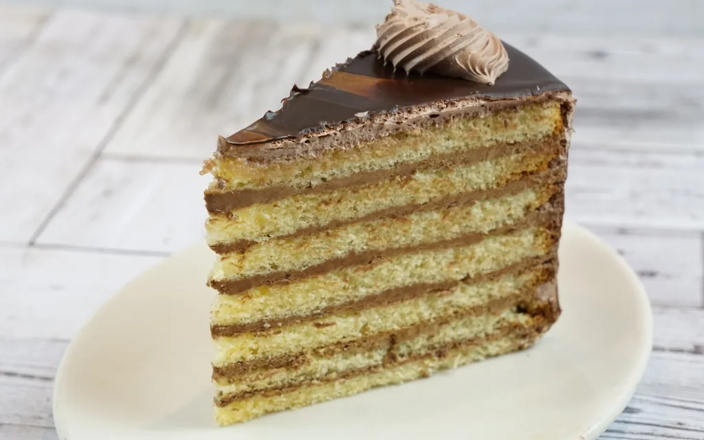 Slice of 7 layer cake showing thin chocolate mousse between seven vanilla layers, one of our mousse-filled cakes